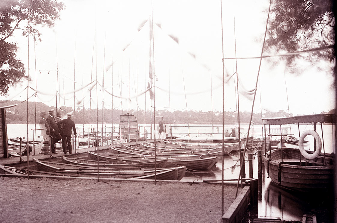 6.Havnen ved 25-års jubilæet d. 17. august 1923. Stationen ligner næsten sig selv. Rækværket på broen fik LF forærende i 1917. I 2023 er det stadig det samme rækværk. Det skulle stamme fra en bro ved Næsset, Ved festen i 1923 blev musikken leveret af Christian S. Jacobsens rejsegrammofon, som hans hustru konstant trak op. Hendes navn var Johanne Sofie Jacobsen, hvilket nok ikke siger de fleste noget. Hvis man nævner, at hendes kælenavn var Pohl, så dæmrer det nok hos det fleste. Hun har nemlig lagt navn til Pohls Banke på Furesøen.