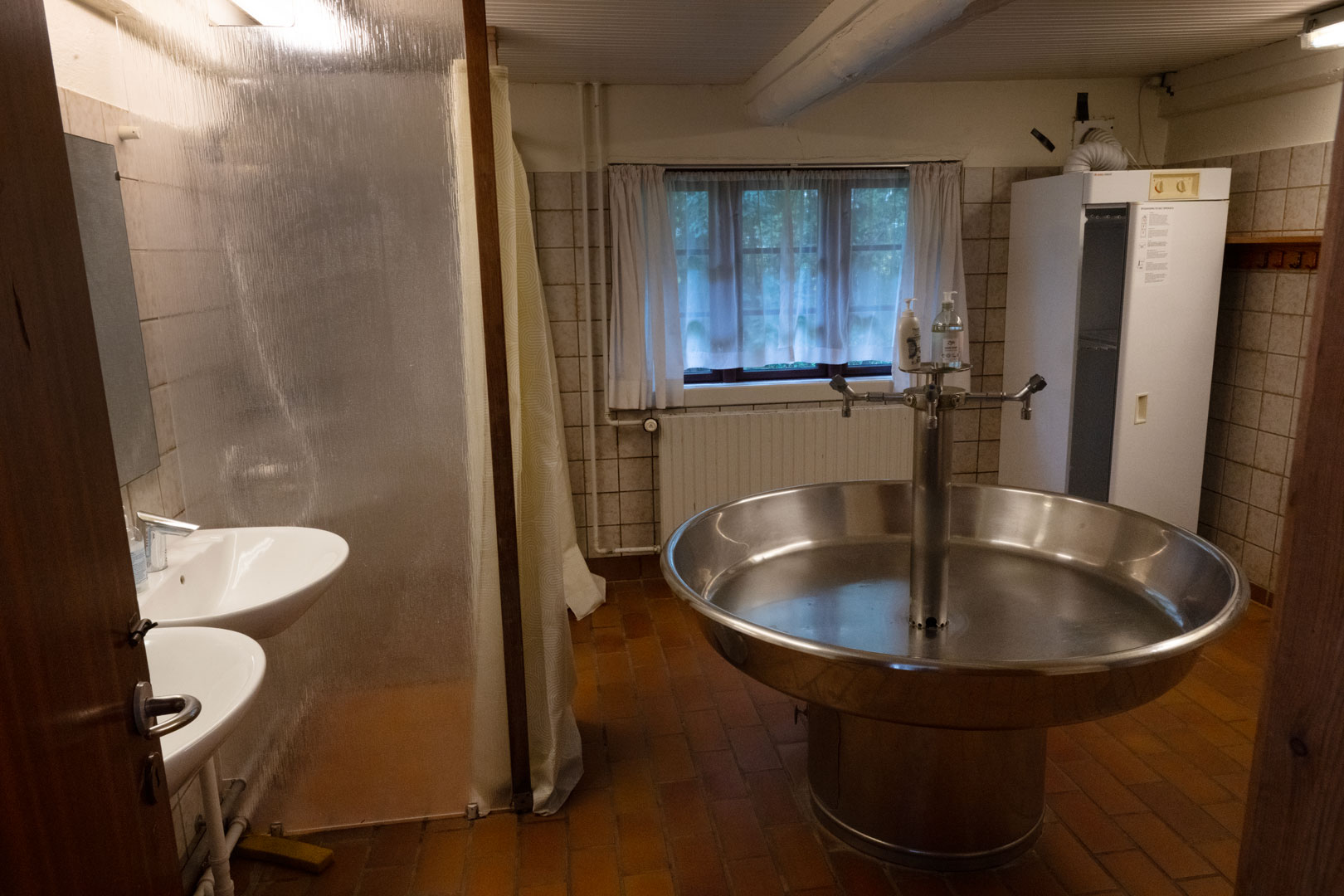 Ved siden af sovesalen er der et stort vaskerum med to brusekabiner og to toiletter samt et tørreskab.